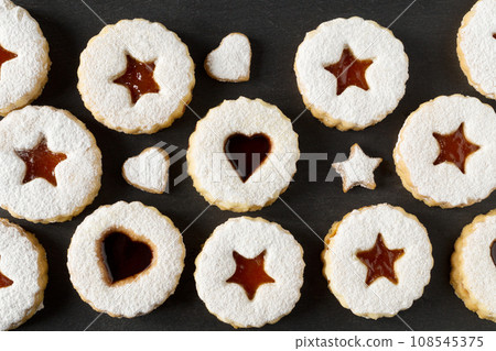 Linzer cookies with apricot jam sprinkled with powdered sugar on a black background. Festive dessert. Top view 108545375