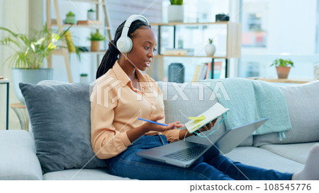 African woman, student and laptop for online course on sofa, headphones and notes with thinking in home. Girl, reading and ideas with notebook, computer or headphones for study on video call on couch 108545776