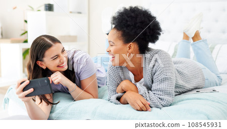 Phone, social media and woman friends laughing on bed together while looking at an internet meme. Smile, diversity and comedy with funny young people joking in the bedroom of a home in the morning 108545931
