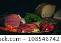 Whole and sliced bresaola on a metal round tray with tomatoes, garlic and bread 108546742