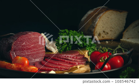 Whole and sliced bresaola on a metal round tray with tomatoes, garlic and bread Whole and sliced bresaola on a metal round tray with tomatoes, garlic and bread 108546742