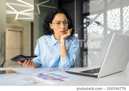 Upset frustrated financial woman checking paper reports, businesswoman behind paperwork inside office, using calculator and laptop to check and analyze report. 108546776