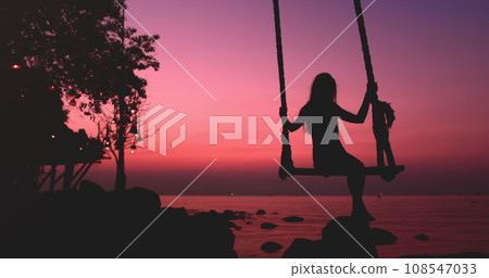 Woman silhouette sway on wooden rope swing against bright pink sunset. Vacation on beautiful seacoast. Travel, tourism, holiday on paradise Thailand Island. Nature landscape in sunrise. 108547033