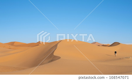 Unidentified tourist walking on sand dunes of Sahara Desert in northern Africa, a vast expanse of sand and dunes that stretches as far as the eye can see. 108547071