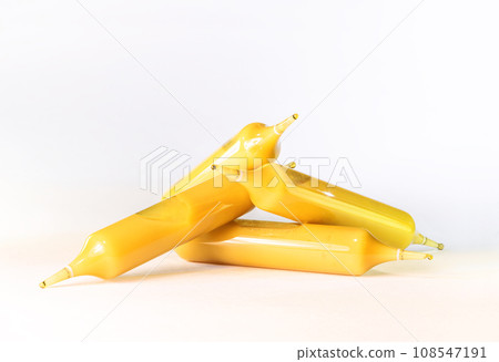 Vials or ampoules containing golden royal jelly are stacked on a white background. 108547191