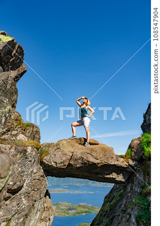 Brave traveler woman standing on hanging stone between rocks. Djevelporten in Norway Lofoten islands 108547904