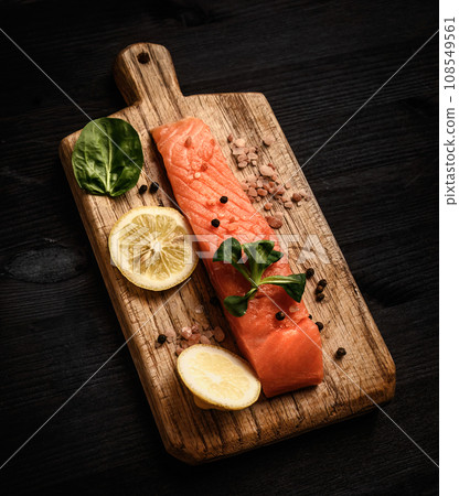 Raw red fish salmon fillet with herbs and lemon on a cutting board ready for cooking healthy dinner Raw red fish salmon fillet with herbs and lemon on a cutting board ready for cooking healthy dinner 108549561