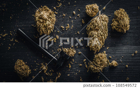 Dried CBD cannabis buds and a metal smoking pipe on a dark wooden background 108549572