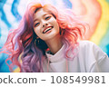 a woman with bright pink hair smiles while posing in front of a rainbow colored background 108549981