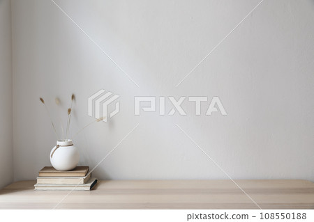 Elegant Scandinavian interior. White ball vase with dry grass, lagurus bouquet on old books. Empty wall background. Modern living room, home office. Minimal moody autumn decor in cozy apartment. 108550188
