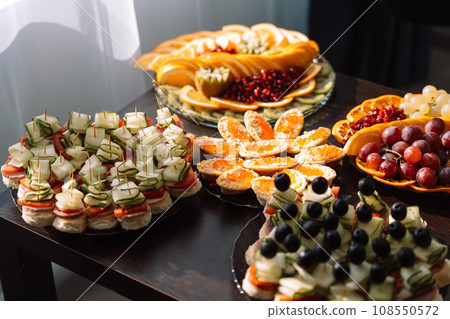Cold appetizers and sliced fruits in plates on a small table Cold appetizers and sliced fruits in plates on a small table 108550572