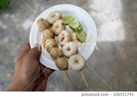 Someone's hand holding a white plate of pork balls and fish balls each. 108551741