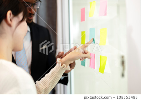 Happy multiethnic business team meeting pointing at post it notes on glass board. Happy multiethnic business team meeting pointing at post it notes on glass board. 108553483