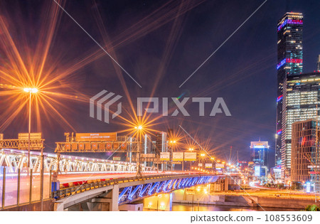 The scyscrapers of the Moscow City at night and the Dorogomilovsky bridge with illumination. Translation of text - street names 108553609