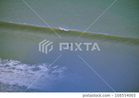 A surfer rides a wave of the sea. View from the height of a multi-storey building. A surfer rides a wave of the sea. View from the height of a multi-storey building. 108554003