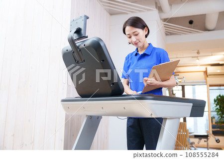 Female staff checking training machines at a sports gym Female staff checking training machines at a sports gym 108555284