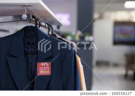 Close up of classic formal jacket with red Black Friday price tag hanging on cloth rack in empty modern fashion store. Special offers in clothing store during seasonal discount sales 108558127