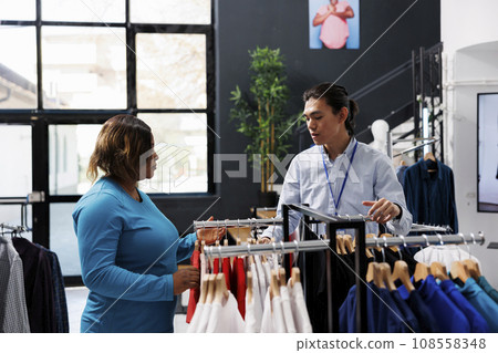Asian employee discussing with woman shopper in modern boutique, shopping for fashionable merchandise. Shopaholic customer buying stylish clothes, looking at new fashion collection Asian employee discussing with woman shopper in modern boutique, shopping for fashionable merchandise. Shopaholic customer buying stylish clothes, looking at new fashion collection 108558348