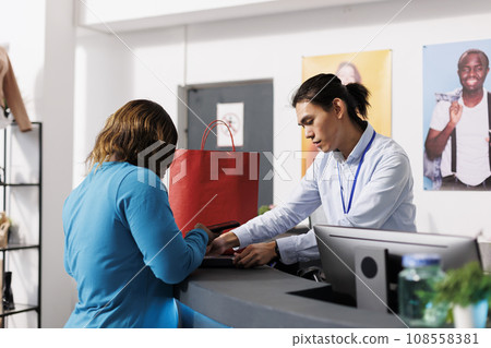 African american customer paying for clothes at counter desk in clothing store, putting credit card on pos. Shopaholic woman shopping for casual wear in modern botique. Fashion concept African american customer paying for clothes at counter desk in clothing store, putting credit card on pos. Shopaholic woman shopping for casual wear in modern botique. Fashion concept 108558381