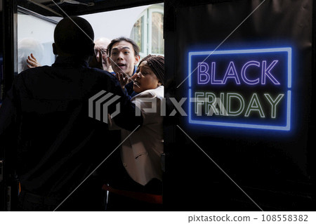 People going crazy for Black Friday deals. Shopping mall security officer managing crowd control, pushing back anxious mad shoppers trying to break into retail store before it opens People going crazy for Black Friday deals. Shopping mall security officer managing crowd control, pushing back anxious mad shoppers trying to break into retail store before it opens 108558382