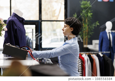 Stylish worker arranging blue shirt on mannequin, preparing boutique for opening. Caucasian woman working at store visual, waiting for customers to come and buy trendy clothes. Fashion concept 108558384