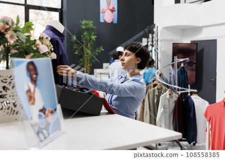 Shopping mall worker preparing store for opening, arranging fashionable merchandise on mannequin. Stylish woman waiting for customers to come and buy trendy clothes and accessories 108558385