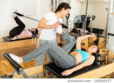 Trainer controlling movements of woman doing pilates on reformer Trainer controlling movements of woman doing pilates on reformer 108560317