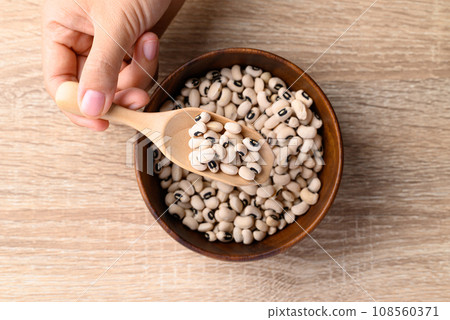 Black eye peas or cowpeas in bowl with spoon holding by hand on wooden background 108560371