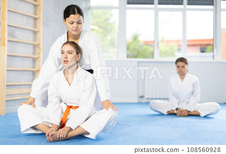 Girl before training martial arts performs stretching butterfly with couch help to warm up muscles. Girl before training martial arts performs stretching butterfly with couch help to warm up muscles. 108560928