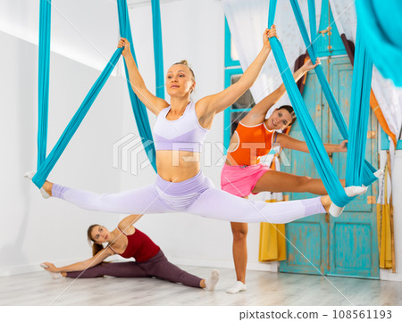 Fit woman doing split on suspended hammocks during antigravity yoga workout Fit woman doing split on suspended hammocks during antigravity yoga workout 108561193