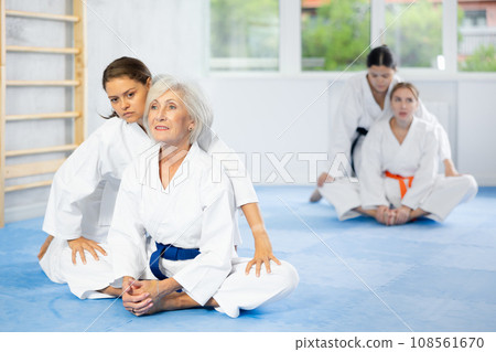 Elderly woman in kimono performing butterfly stretch with help of female coach 108561670