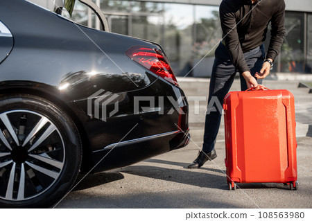 Chauffeur packs a suitcase into luxury car 108563980