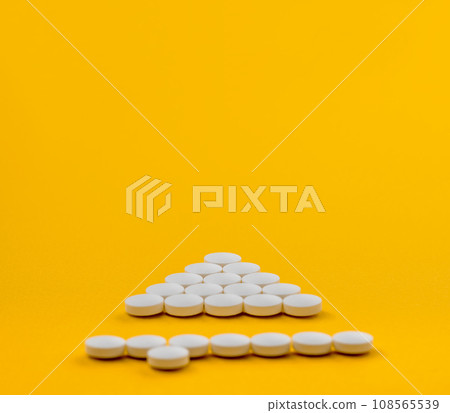 White medical pills in shape of upwards arrow on yellow background. Medicine, pills background. Treatment. Prevention. White medical pills in shape of upwards arrow on yellow background. Medicine, pills background. Treatment. Prevention. 108565539