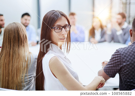 girl posing for the camera sitting at a round table against the background of her colleagues 108565882