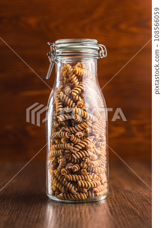 Raw whole grain fusilli pasta. Uncooked pasta in jar on wooden table. Raw whole grain fusilli pasta. Uncooked pasta in jar on wooden table. 108566059