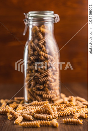 Raw whole grain fusilli pasta. Uncooked pasta in jar on wooden table. 108566061