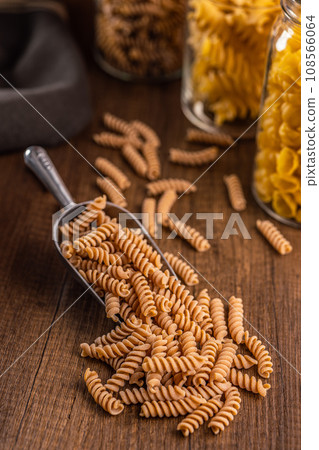 Raw whole grain fusilli pasta. Uncooked pasta in scoop on wooden table. 108566064