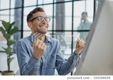 Excited modern businessman sitting at office desk and rejoicing his success Excited modern businessman sitting at office desk and rejoicing his success 108566699