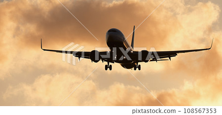 Silhouette passenger airplane. Front of silhouette airplane is flying in the orange sky with clouds, Passenger aircraft is landing. Commercial plane Silhouette passenger airplane. Front of silhouette airplane is flying in the orange sky with clouds, Passenger aircraft is landing. Commercial plane 108567353