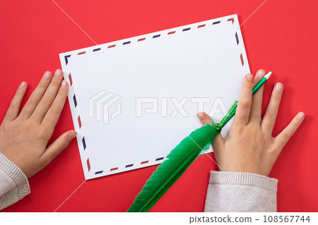 Childs hands with a pen in the shape of a feather and an empty mail envelope on a colored background, template for the designer Childs hands with a pen in the shape of a feather and an empty mail envelope on a colored background, template for the designer 108567744