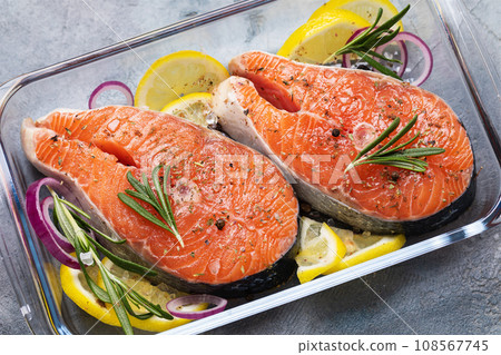 Two fresh raw trout steaks with rosemary, lemon, onion and pepper in a clear glass baking dish on the table Two fresh raw trout steaks with rosemary, lemon, onion and pepper in a clear glass baking dish on the table 108567745