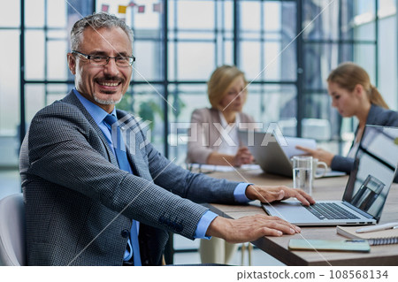 Happy businessman wearing eyeglasses sitting with laptop Happy businessman wearing eyeglasses sitting with laptop 108568134