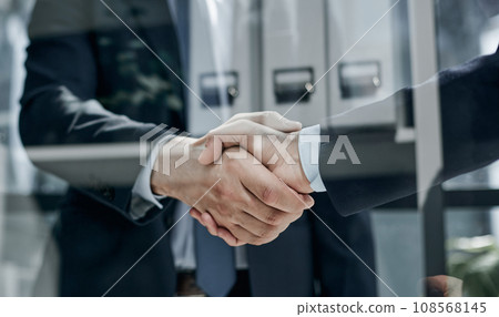 executives shaking hands in front of their manager and a colleague executives shaking hands in front of their manager and a colleague 108568145