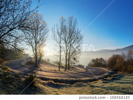 mountain pass in autumn. sun behind the leafless trees on the grassy hills in frost. mist in the valley. blue sky above the distant ridge 108568185