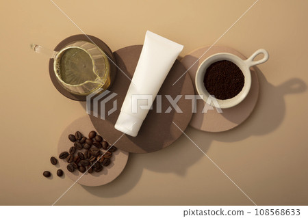 A white plastic bottle displayed on round podiums with coffee beans, coffee powder and glass pot of oil on brown background. Mockup bottle for design. Advertising photo 108568633