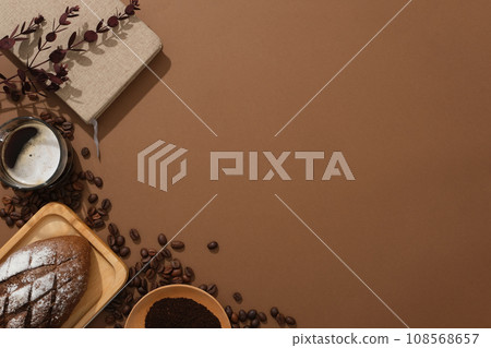 Creative background for advertising and branding product with coffee. Against a brown background, glass cup of coffee, bread and coffee powder decorated on left corner. Space for design  108568657