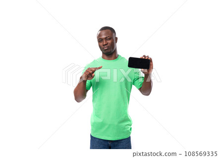 young leader african man dressed in a green t-shirt and jeans shows the screen of a mobile phone young leader african man dressed in a green t-shirt and jeans shows the screen of a mobile phone 108569335