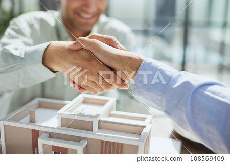 handshake against the background of a model of a house under construction. client and designer 108569409