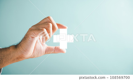 A hand holds a plus icon for medical care, signifying advantages. Health insurance health concept featuring access to welfare health and spacious copy area. 108569700