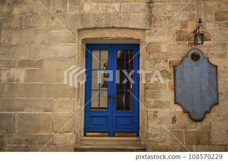 Building facade, blue door, lantern and wooden notice board on wall outdoors 108570229